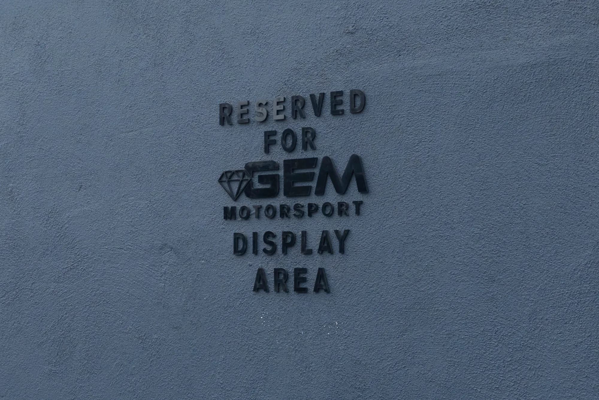 Raised wall lettering on the GEM campus reading “Reserved for GEM Motorsport display area”, with the GEM diamond mark