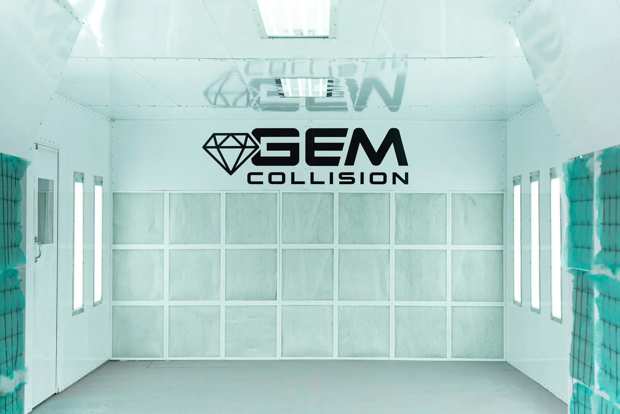 The GEM Collision paint booth interior, lit for refinishing, with the GEM Collision logo on the back wall